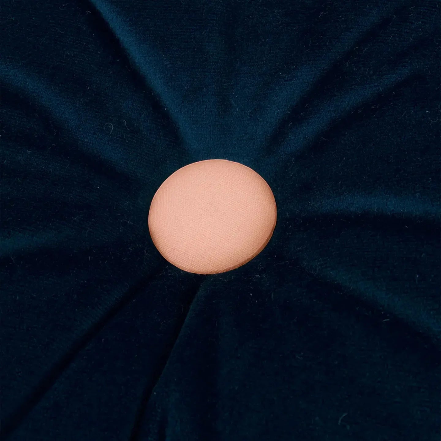 A round, night blue cushion with a contrasting pink button in the center, made from eco-velvet fabric, available in Singapore