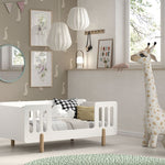 A white toddler bed with natural wood legs and surrounding railing, available in Singapore