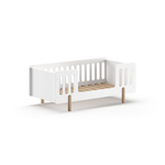 A white toddler bed with natural wood legs and surrounding railing, available in Singapore