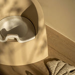 A beige Quax potty with a white inner bowl and high backrest, designed for toddlers.