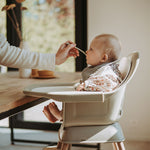 A Quax Ultimo High Chair in stone color with a modern design, featuring a high seat and adjustable legs, suitable for babies and toddlers.