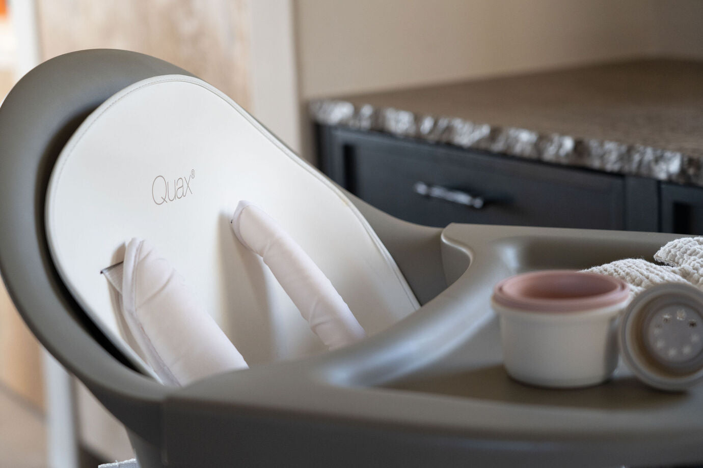 A Quax Ultimo High Chair in stone color with a modern design, featuring a high seat and adjustable legs, suitable for babies and toddlers.